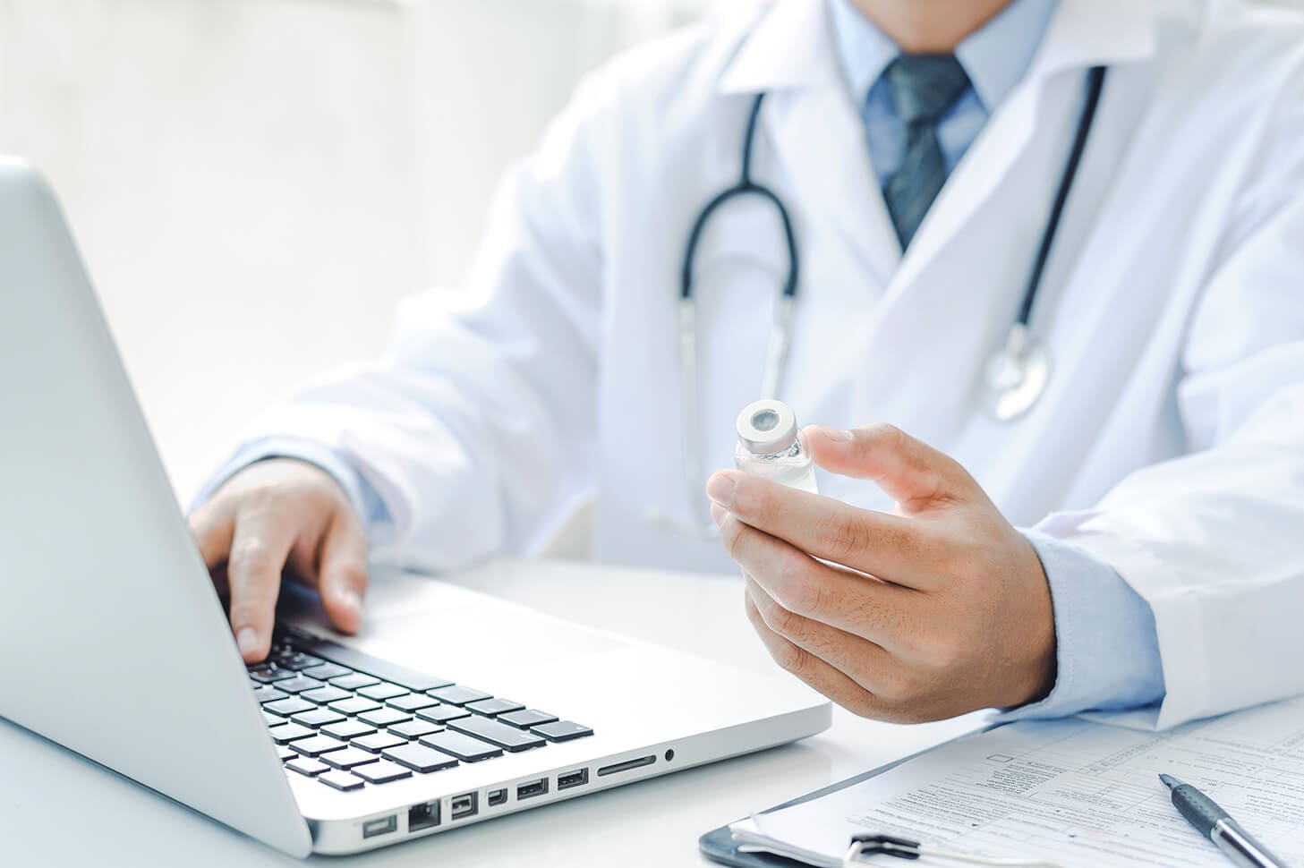 Doctor holding medicine vial near laptop.