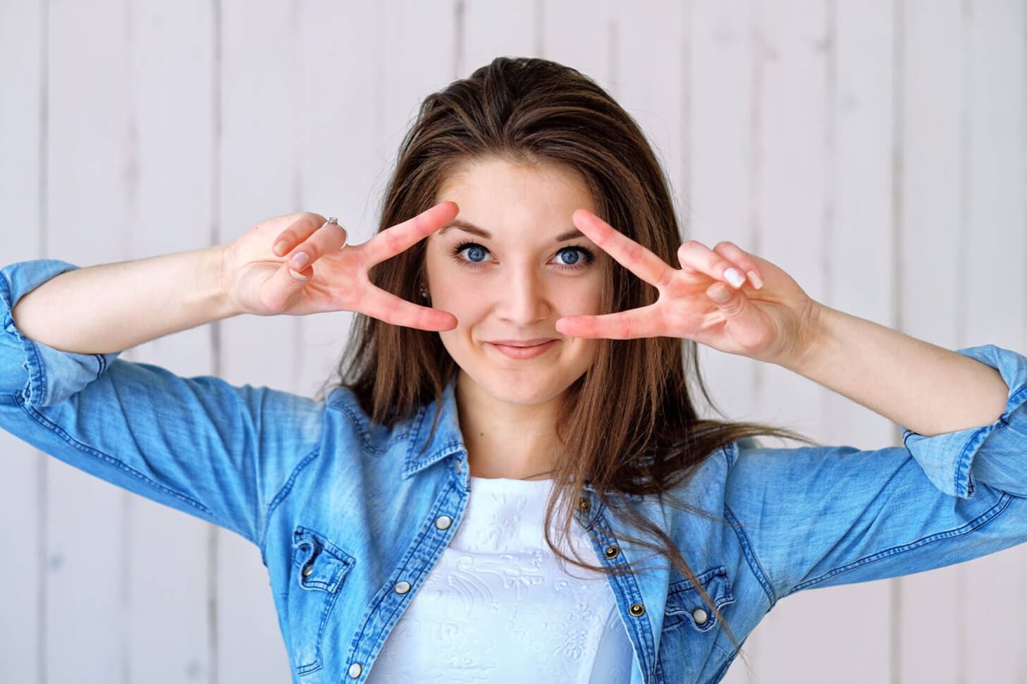 Smiling woman in denim makes peace sign.